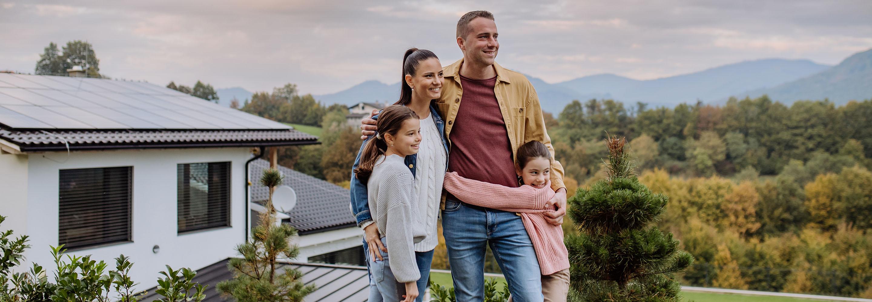 Familie steht vor einem Haus auf dem eine PV-Anlage angebracht ist