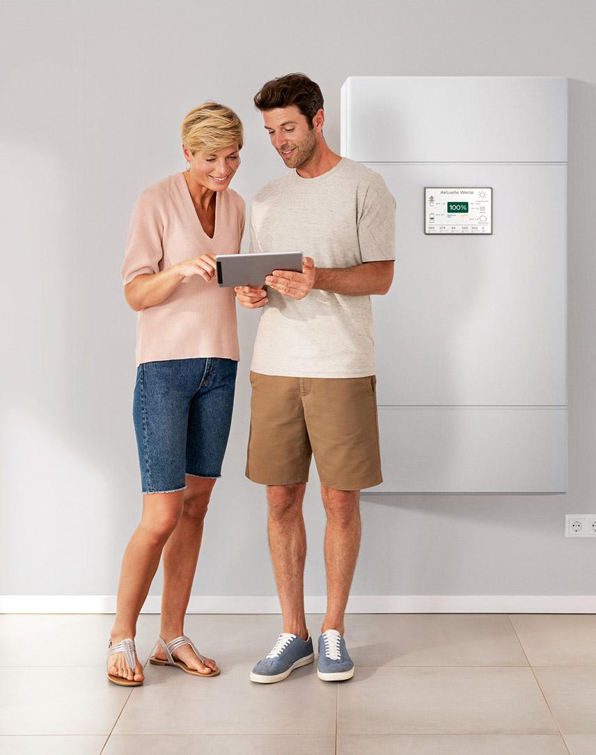 Ein Mann und eine Frau schauen gemeinsam auf ein Tablet vor einem PV-Speicher.