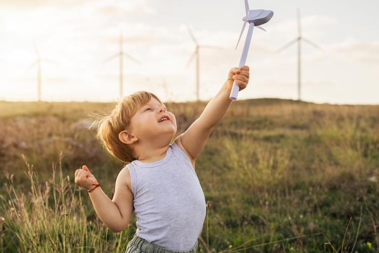 Kleiner Junge spielt mit einem kleinen Windrad, im Hintergrund sind echte Windkraftanlagen