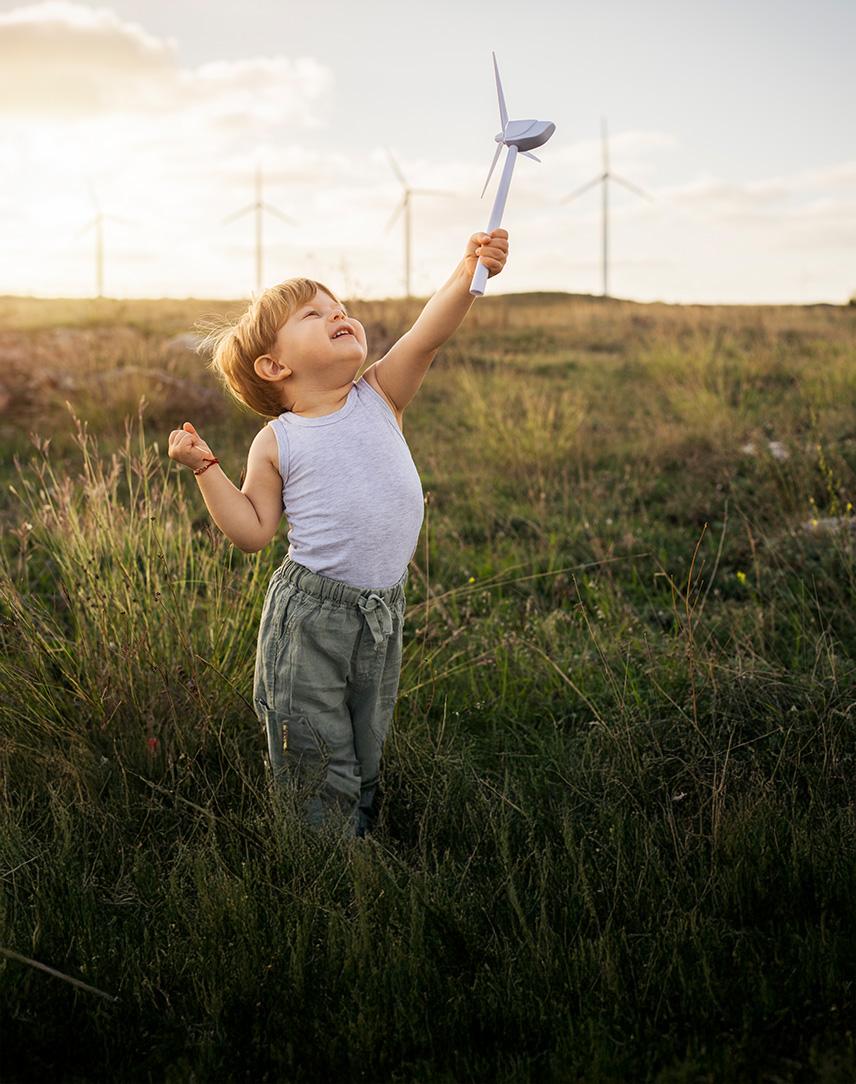 Kleiner Junge spielt mit einem kleinen Windrad, im Hintergrund sind echte Windkraftanlagen