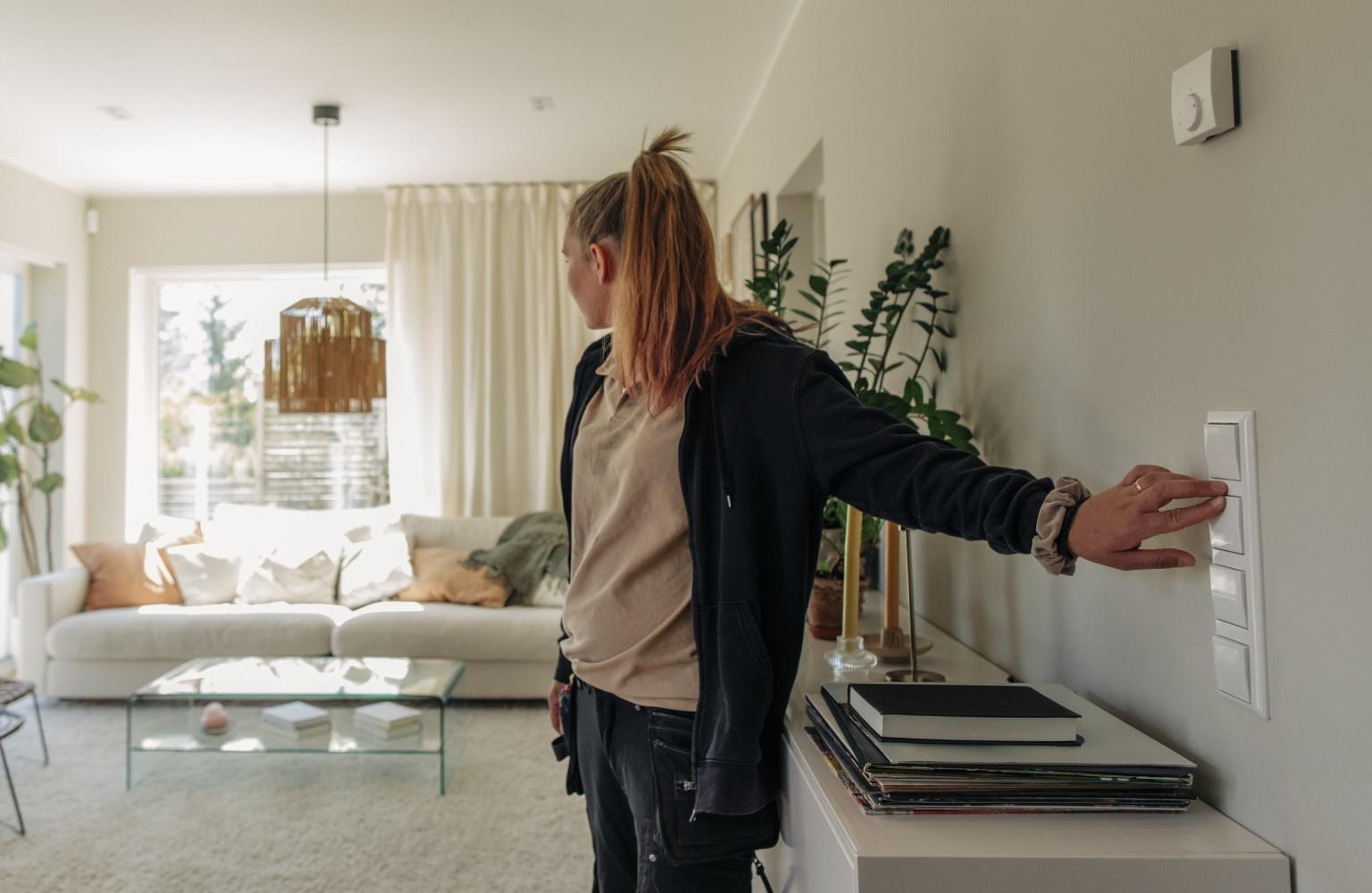 Junge Frau schaltet das Licht in ihrem Wohnzimmer an