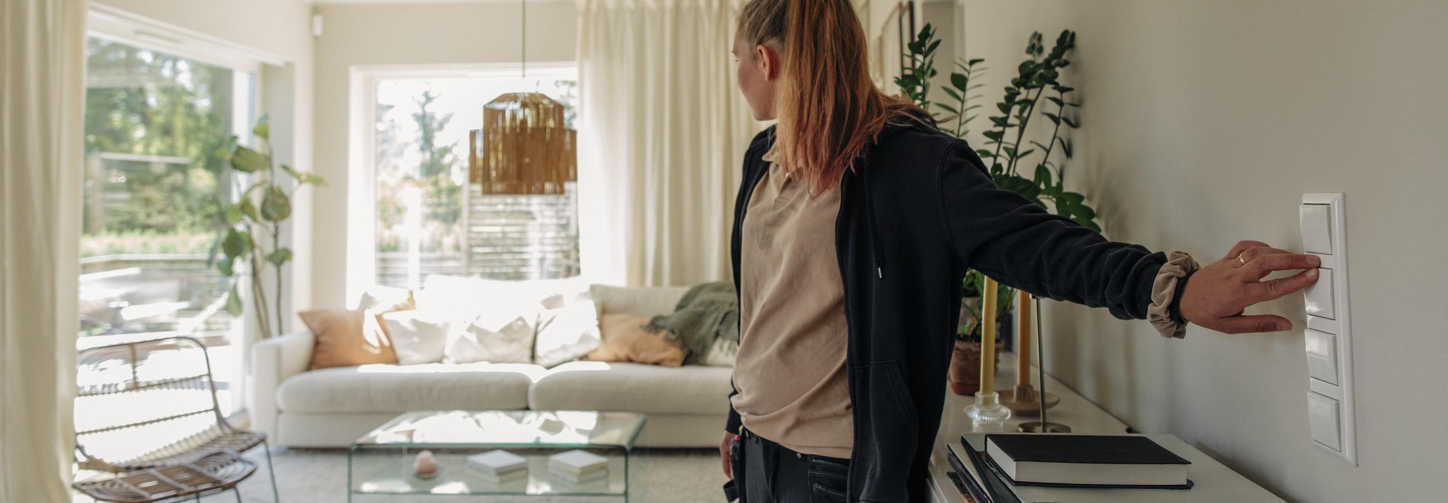 Junge Frau schaltet das Licht in ihrem Wohnzimmer an