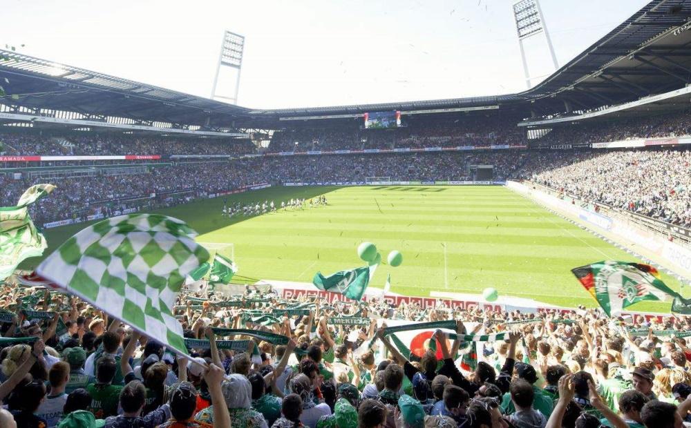 Drei Fußballer von Werder Bremen in Trikots schauen in die Kamera.