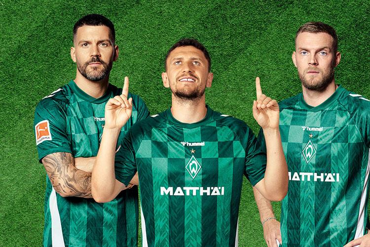 Drei Fußballer von Werder Bremen in Trikots schauen in die Kamera.