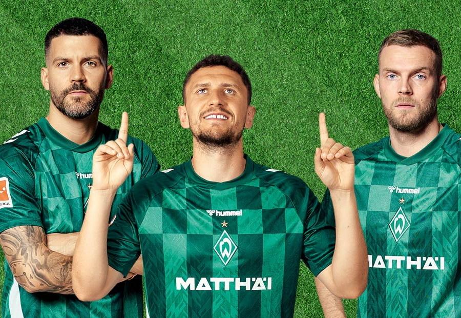 Drei Fußballer von Werder Bremen in Trikots schauen in die Kamera.
