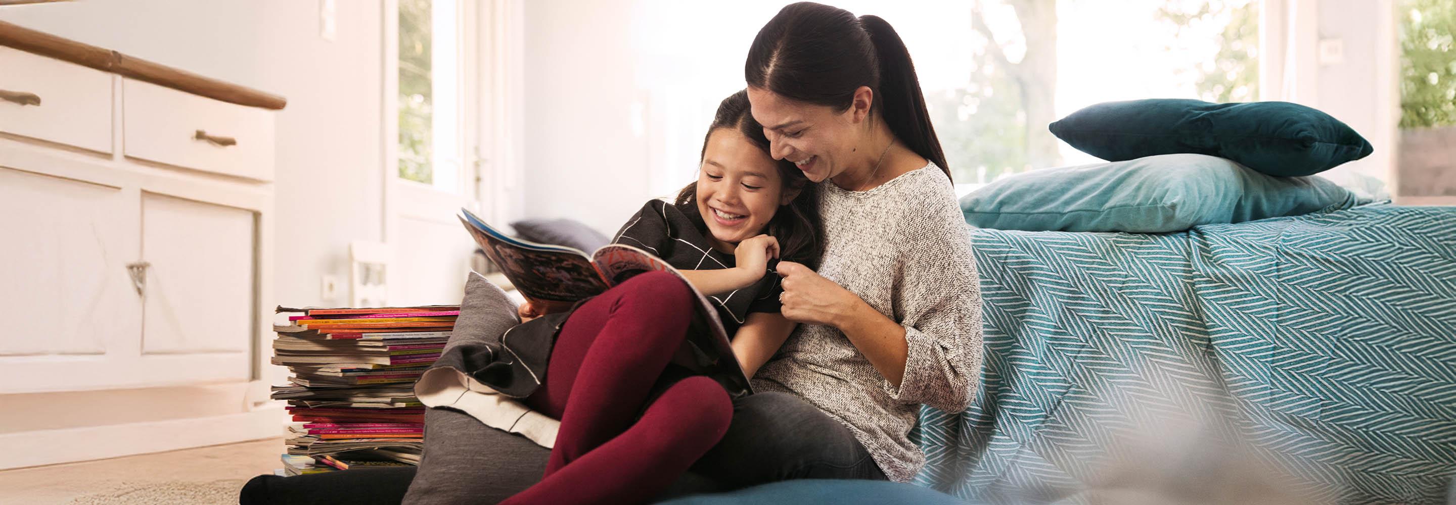 Mutter sitzt mit ihrer Tochter auf der Couch und liest ihr aus Zeitschriften vor