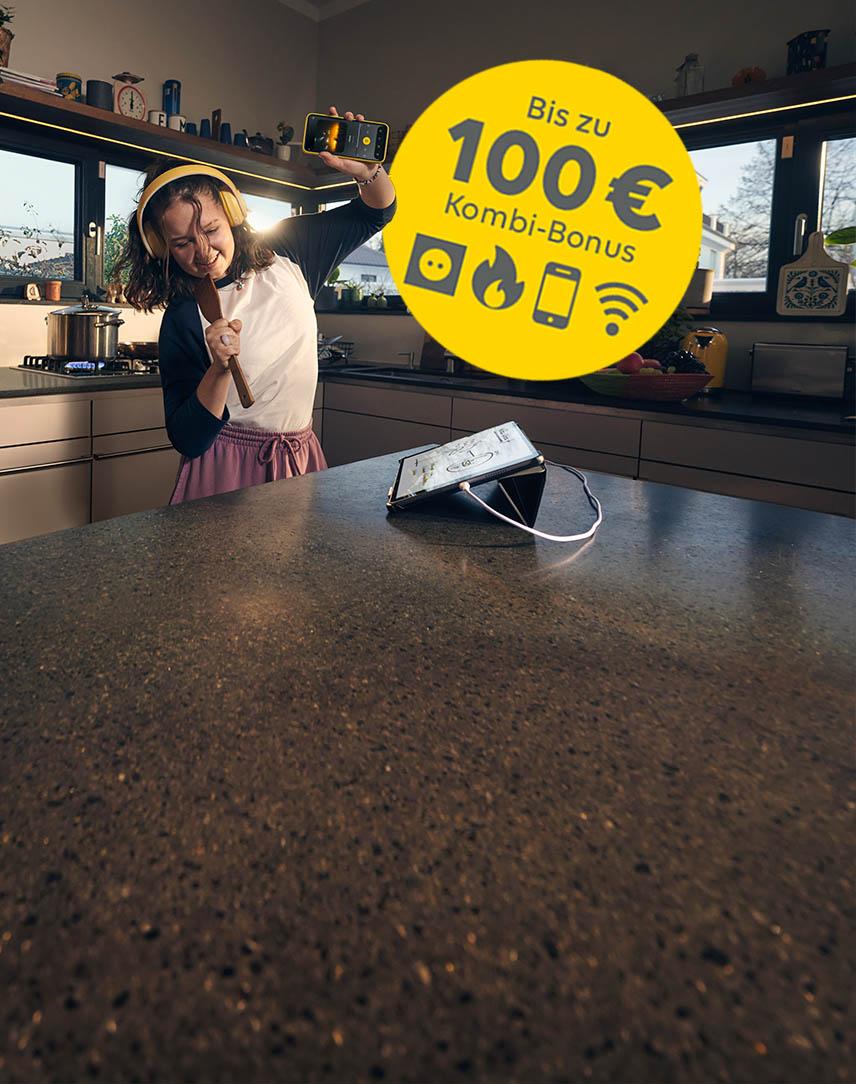 Mädchen singt in der Küche, ein gelber Störer weißt auf 100 Euro Kombibonus hin
