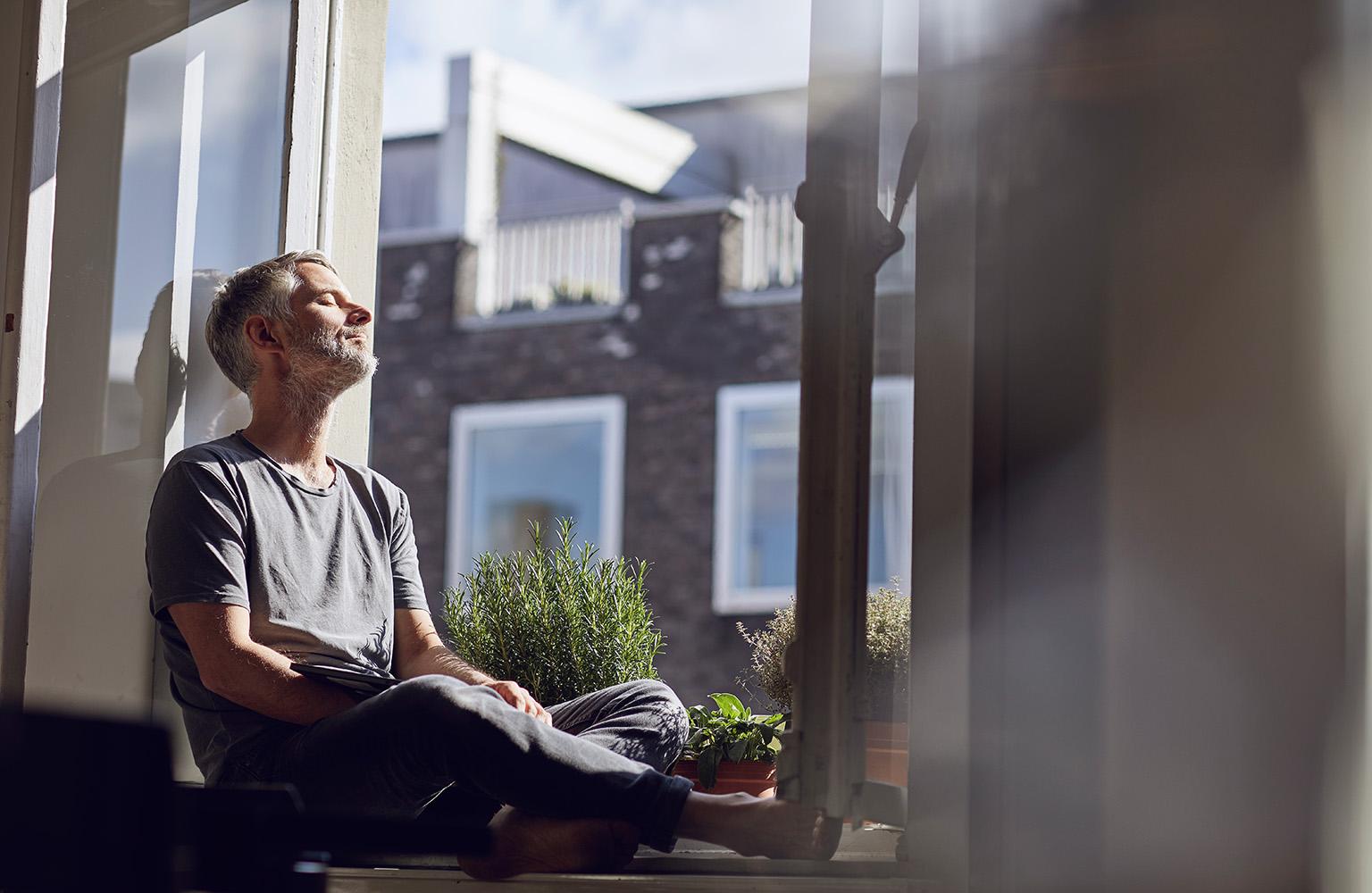 Mann sitzt auf der Fensterbank und schaut in die Sonne