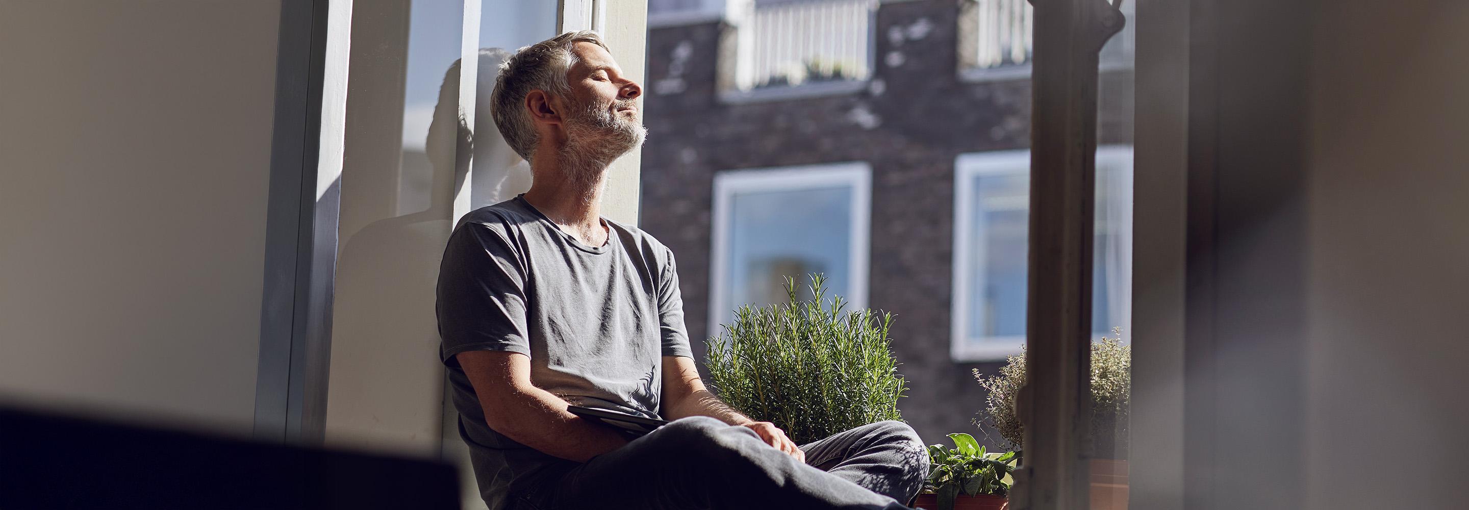 Mann sitzt auf der Fensterbank und schaut in die Sonne