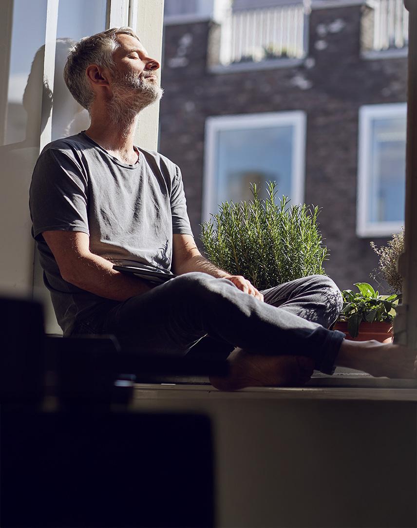 Mann sitzt auf der Fensterbank und schaut in die Sonne