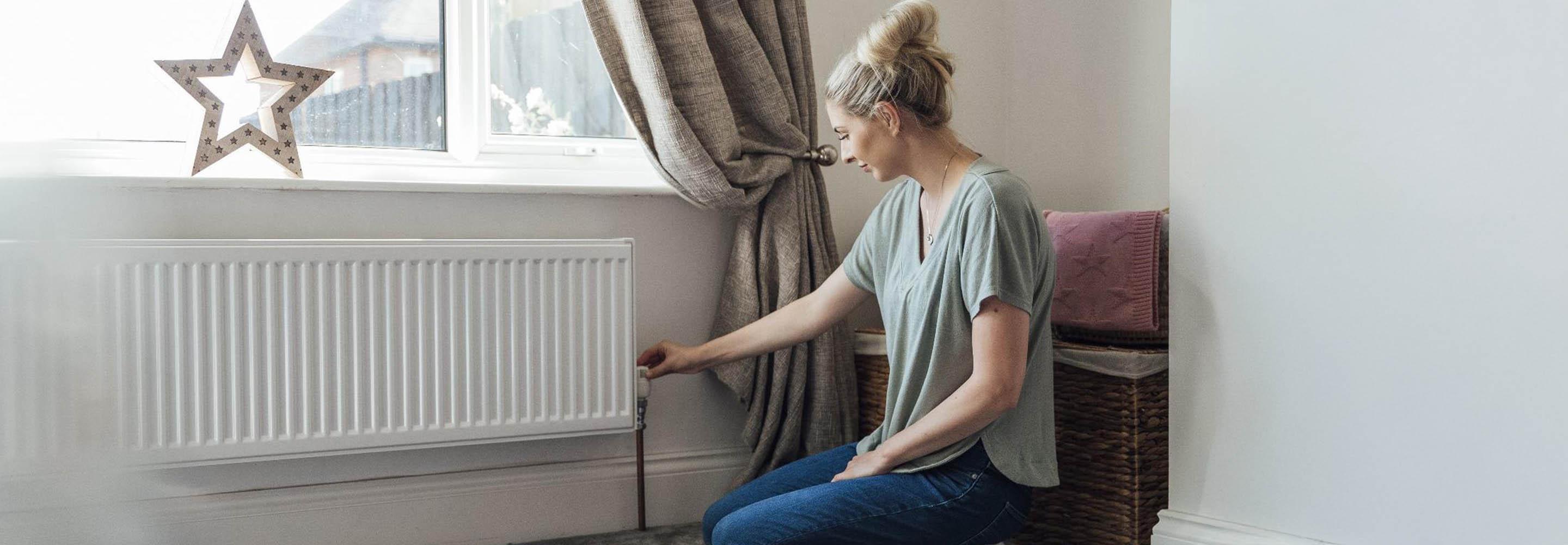 Frau dreht am Thermostat einer Heizung