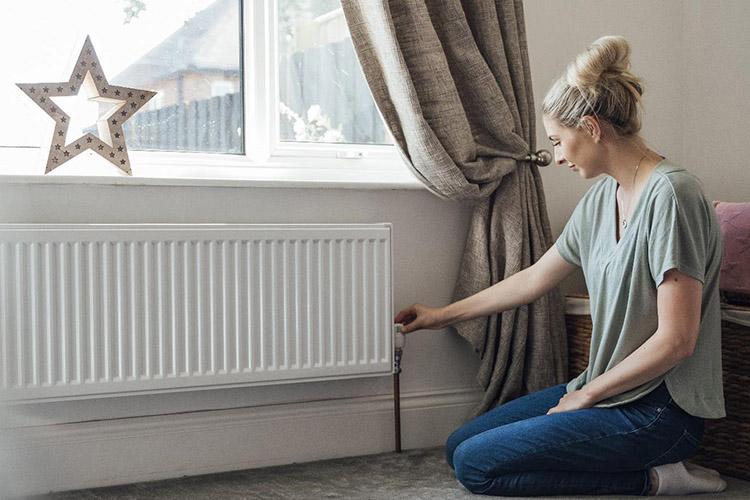 Frau dreht am Thermostat einer Heizung