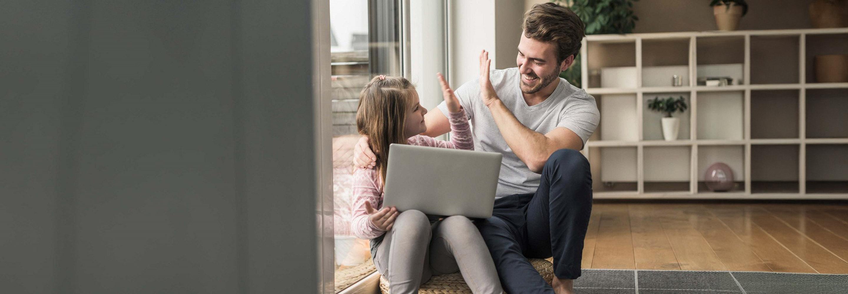 Vater und Tochter mit Laptop auf dem Schoß geben sich ein High-Five