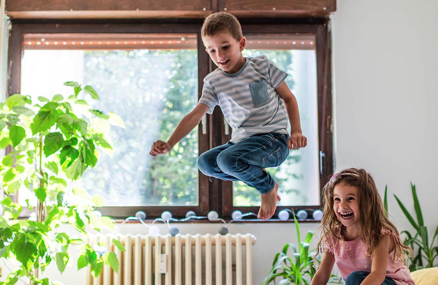 Zwei Kinder turnen und springen im Zimmer vor einer Heizung