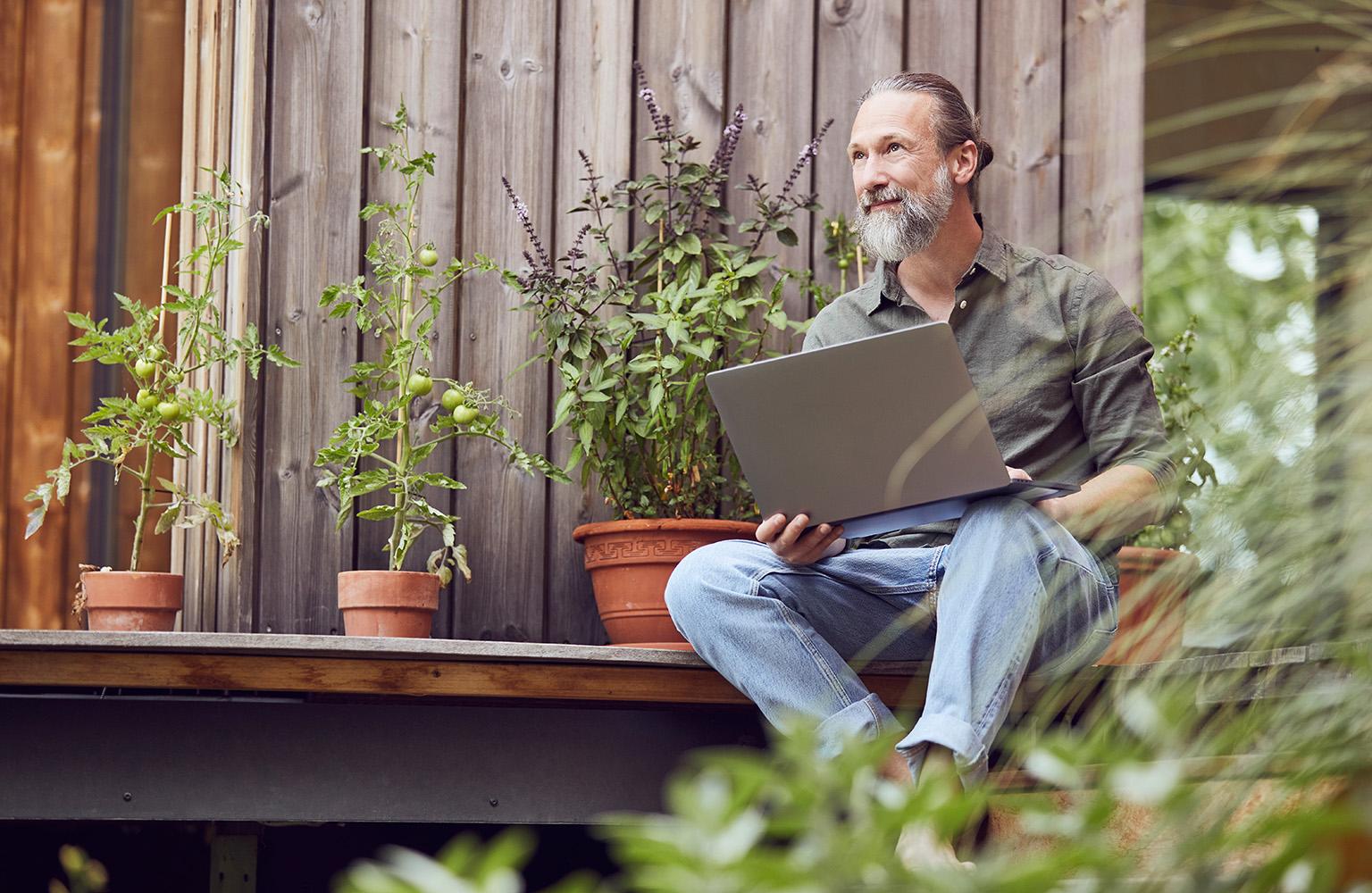 Mann sitzt mit Laptop auf dem Schoß auf der Terrasse