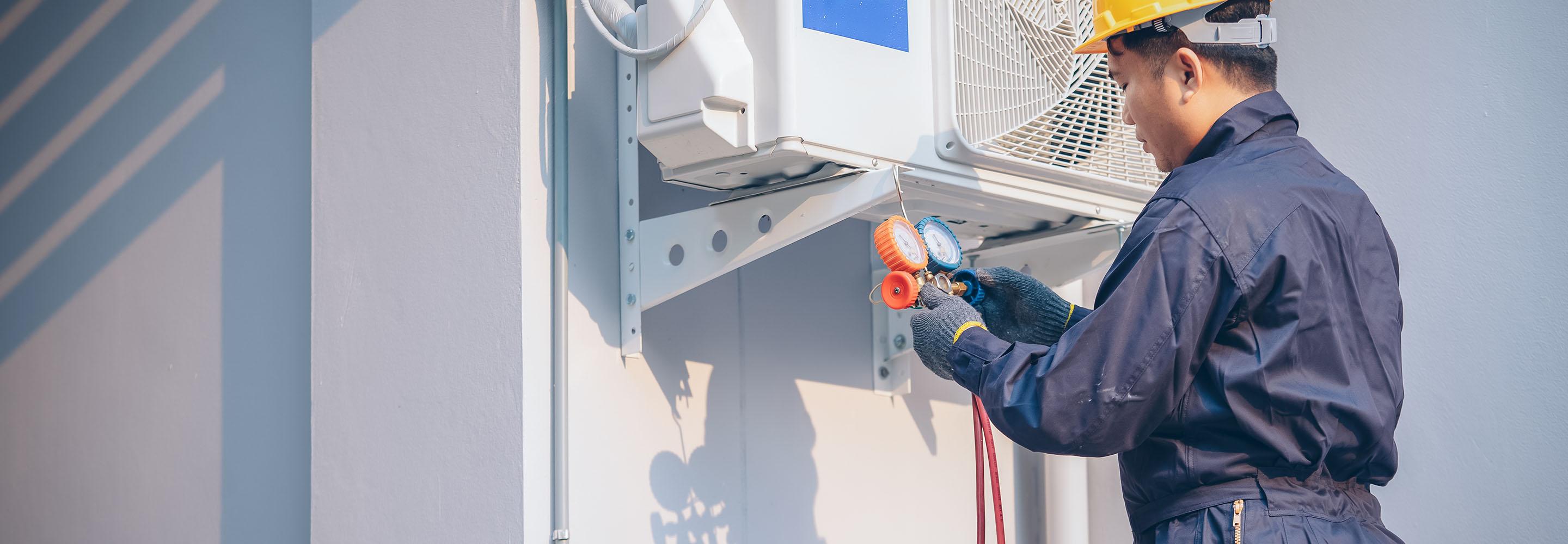 Handwerker mit Bauhelm installiert eine Wärmepumpe an Hauswand