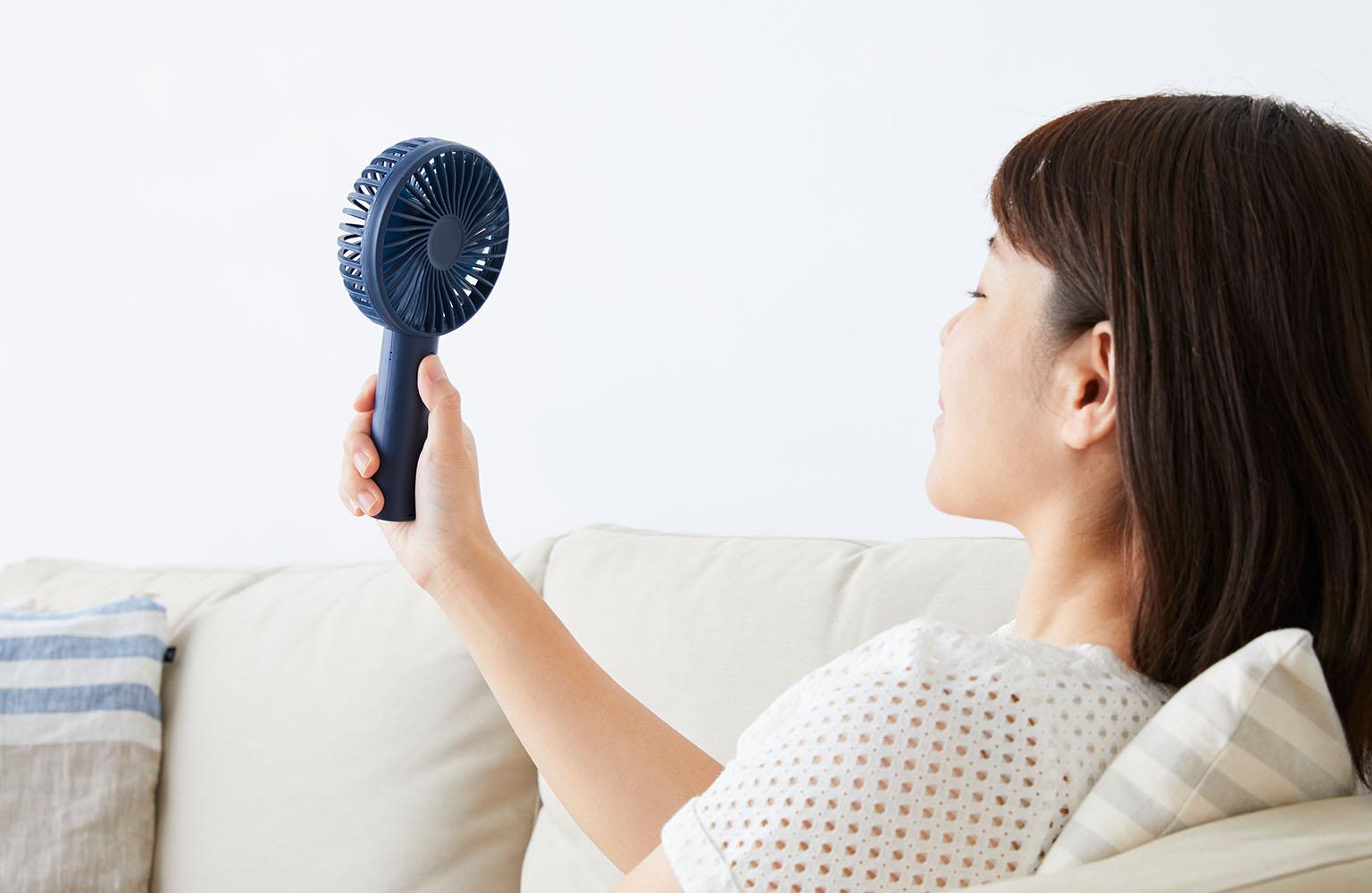 Frau pustet sich mit Handventilator Luft ins Gesicht.
