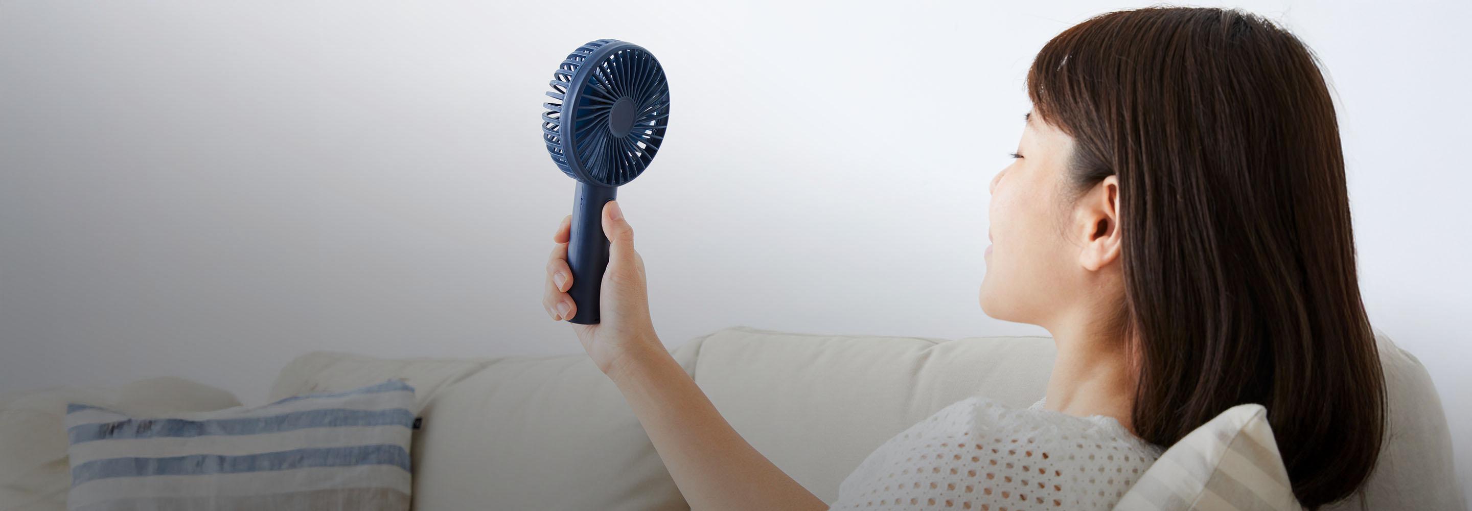 Frau pustet sich mit Handventilator Luft ins Gesicht.