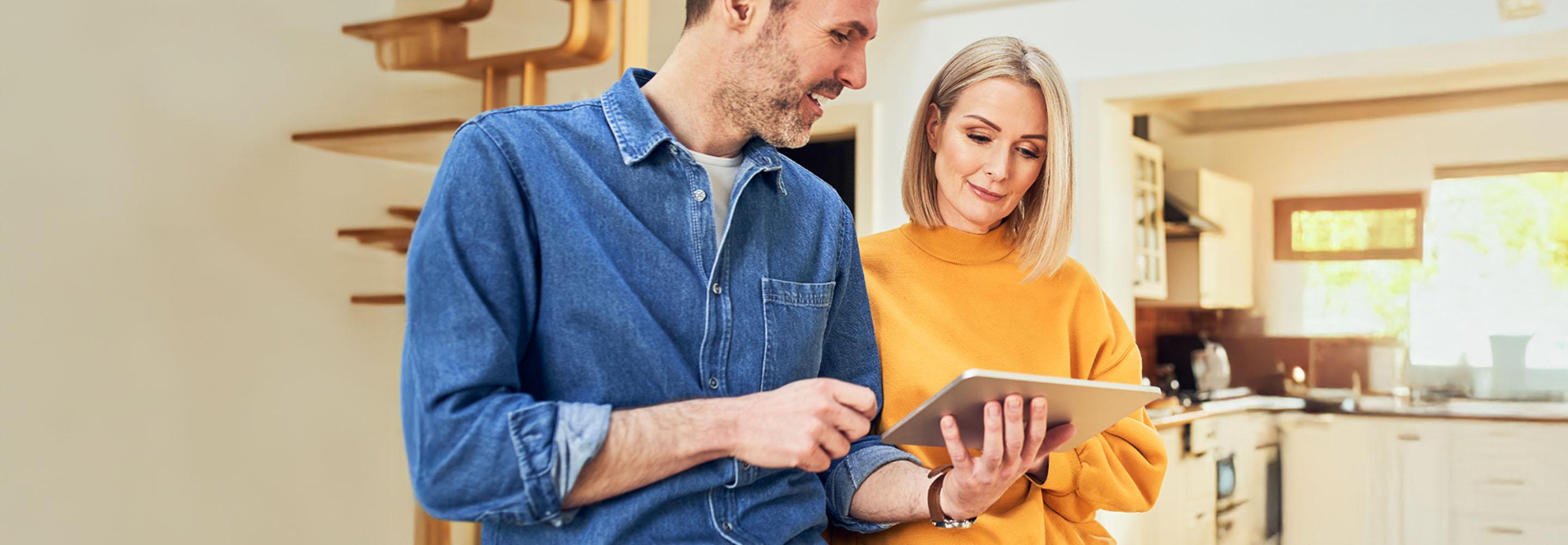 Mann und Frau stehen in der Küche und schauen auf ein Tablet
