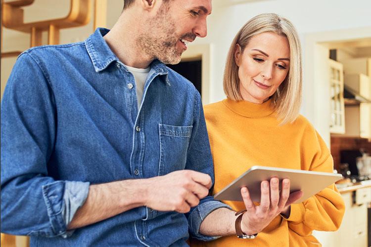 Mann und Frau stehen in der Küche und schauen auf ein Tablet