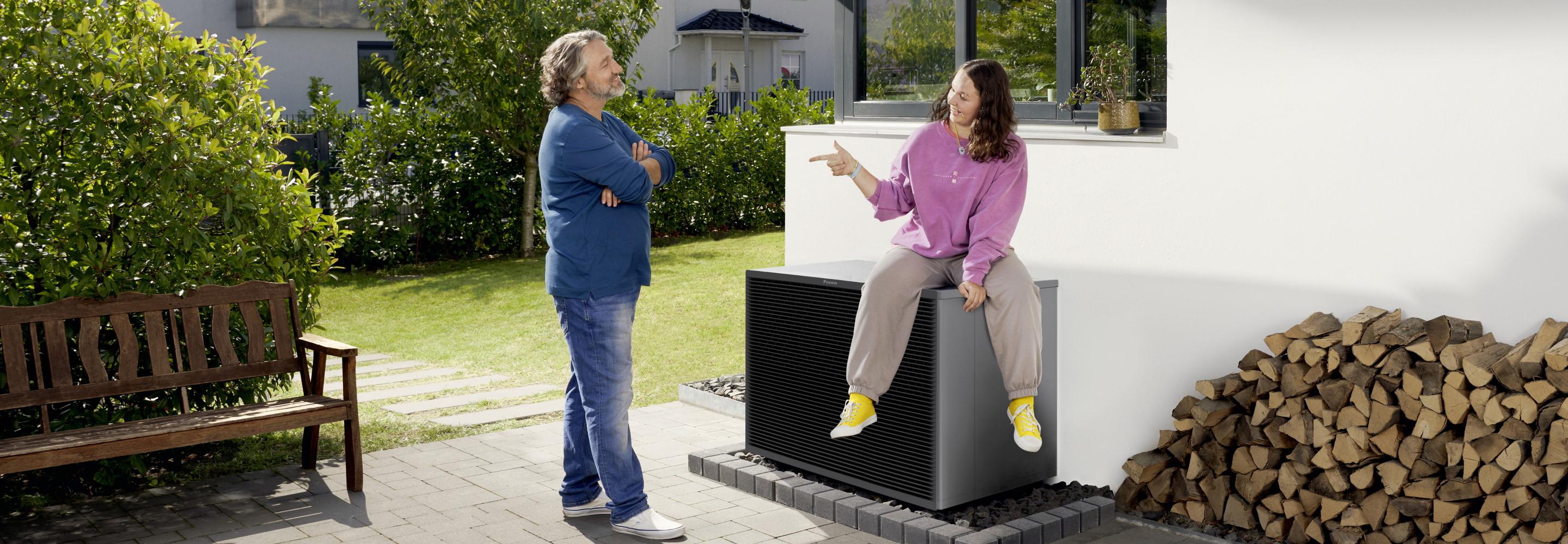 Vater und Tochter, die auf einer Wärmepumpe sitzt, unterhalten sich in ihrem Garten