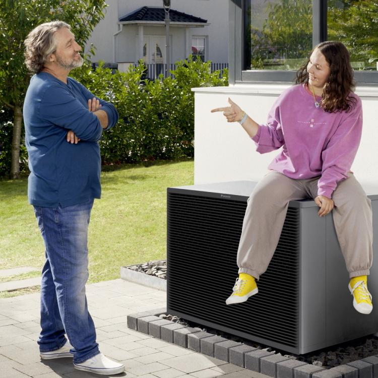 Vater und Tochter, die auf einer Wärmepumpe sitzt, unterhalten sich in ihrem Garten