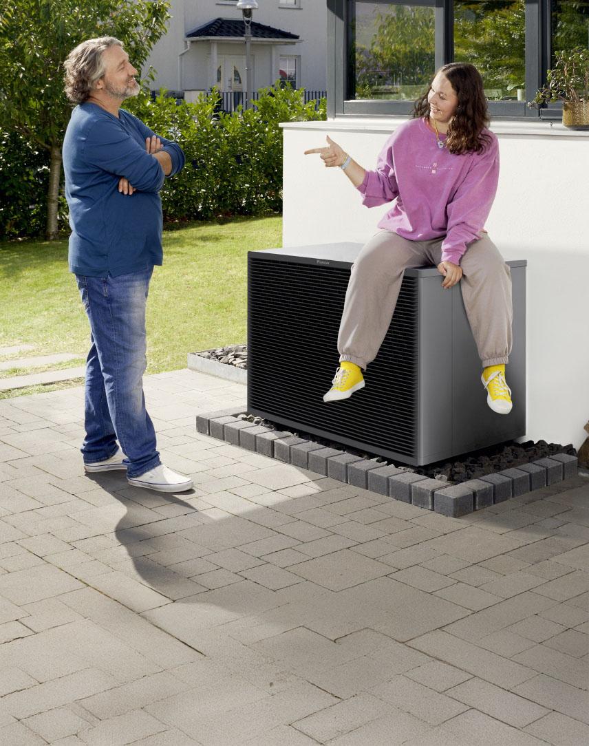 Vater und Tochter, die auf einer Wärmepumpe sitzt, unterhalten sich in ihrem Garten