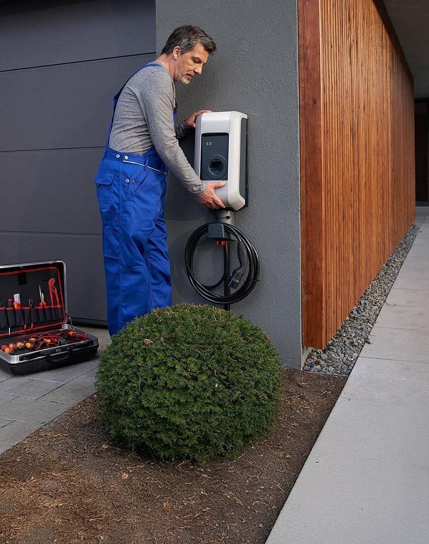 Handwerker bringt Wallbox an Hauswand an.