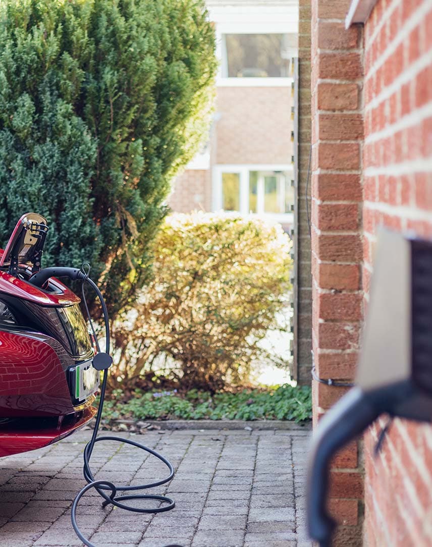 Wallbox an Hauswand, im Hintergrund lädt ein Elektroauto