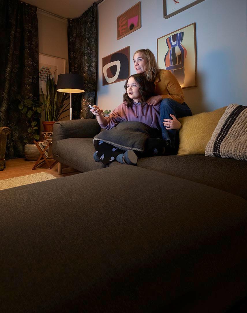 Mutter und Tochter sitzen auf der Couch mit einer Fernbedienung und schauen EWE ZuhauseTV