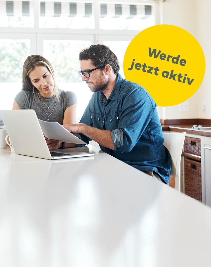 Frau und Mann sitzen vor Laptop mit Unterlagen in der Hand