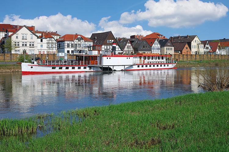 Raddampfer auf der Weser vor einer Fachwerkhäuserkulisse bei Minden.