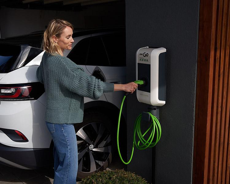 Frau steckt Stecker in Wallbox am Haus.