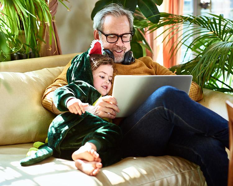 Mann und Kind schauen gemeinsam auf dem Sofa auf einen Laptop-Bildschirm.