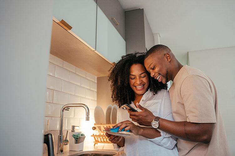 Mann und Frau stehen in der Küche und schauen lachend auf ein Smartphone