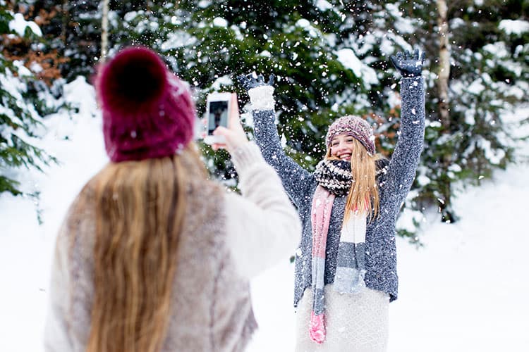 Ein Mädchen fotografiert ein anderes Mädchen mit dem Handy in einer Schneelandschaft