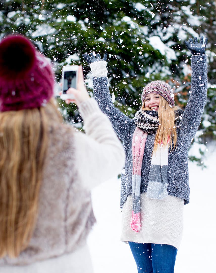 Ein Mädchen fotografiert ein anderes Mädchen mit dem Handy in einer Schneelandschaft