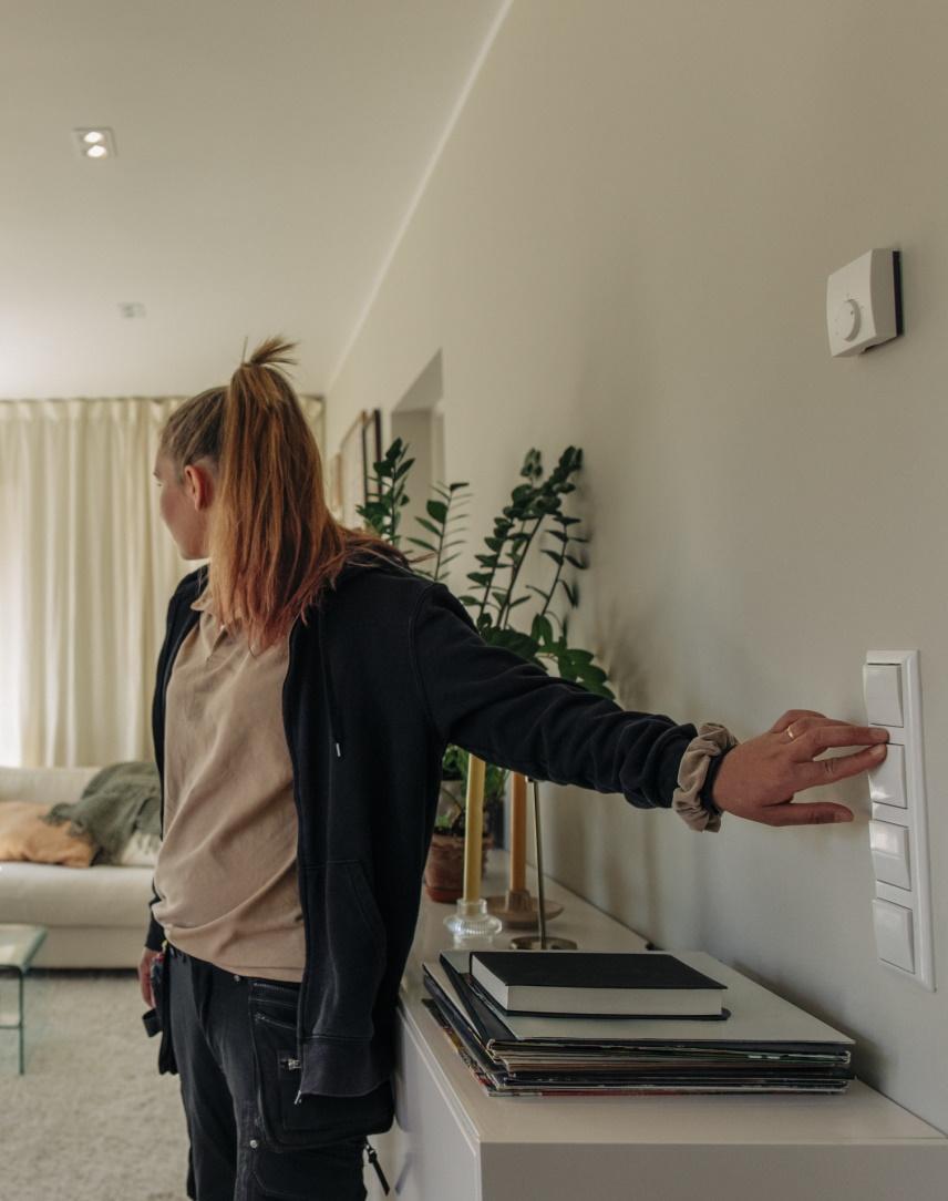 Junge Frau schaltet das Licht in ihrem Wohnzimmer an