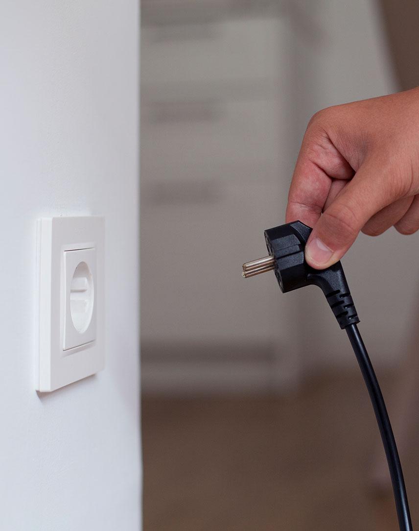 Eine Hand steckt schwarzen Stecker in eine Steckdose