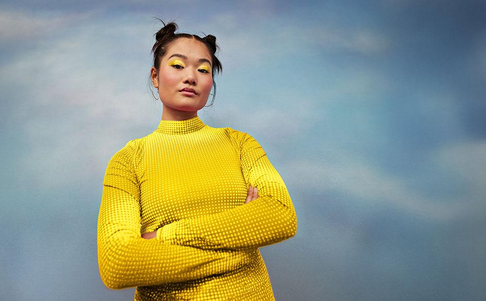 Frau mit verschränkten Armen vor Himmel-Hintergrund.