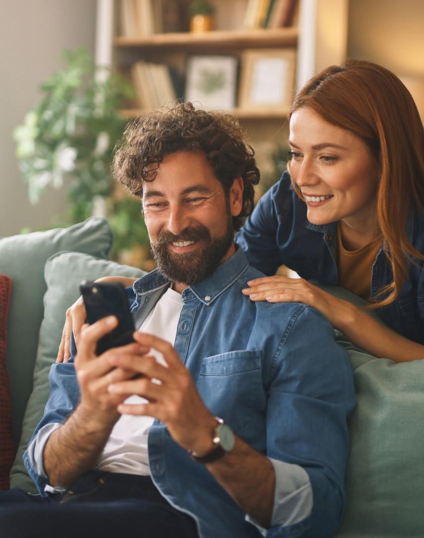 Rothaarige Frau am Schreibtisch schaut auf ihr Smartphone und freut sich