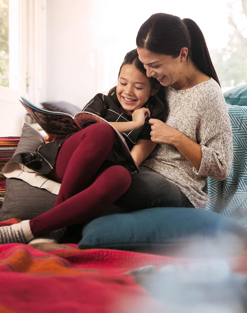 Mutter sitzt mit ihrer Tochter auf der Couch und liest ihr aus Zeitschriften vor