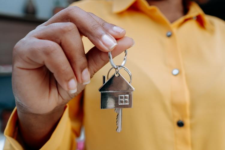 Frau hält einen Schlüssel mit einem Zuhause-Schlüsselanhänger in der Hand