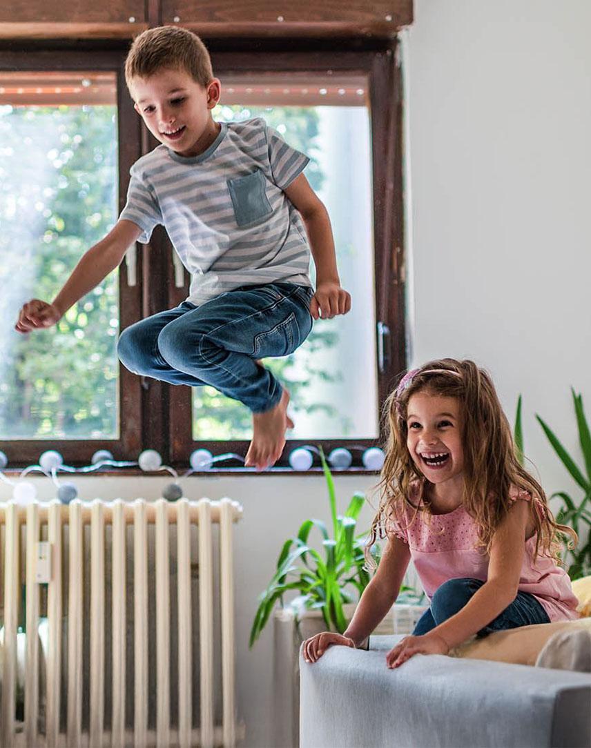 Zwei Kinder turnen und springen im Zimmer vor einer Heizung