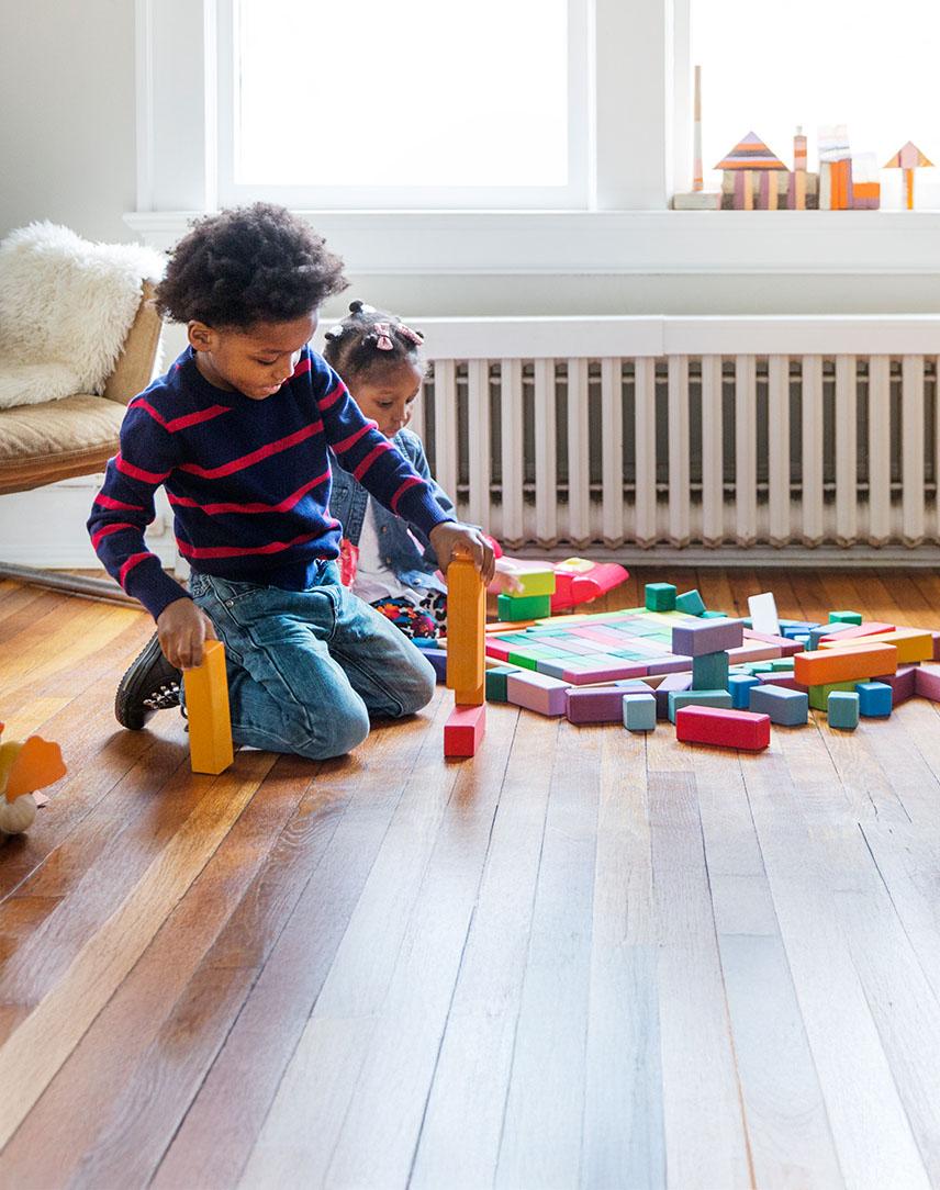 Junge spielt mit Bauklötzen im Wohnzimmer vor einer Heizung