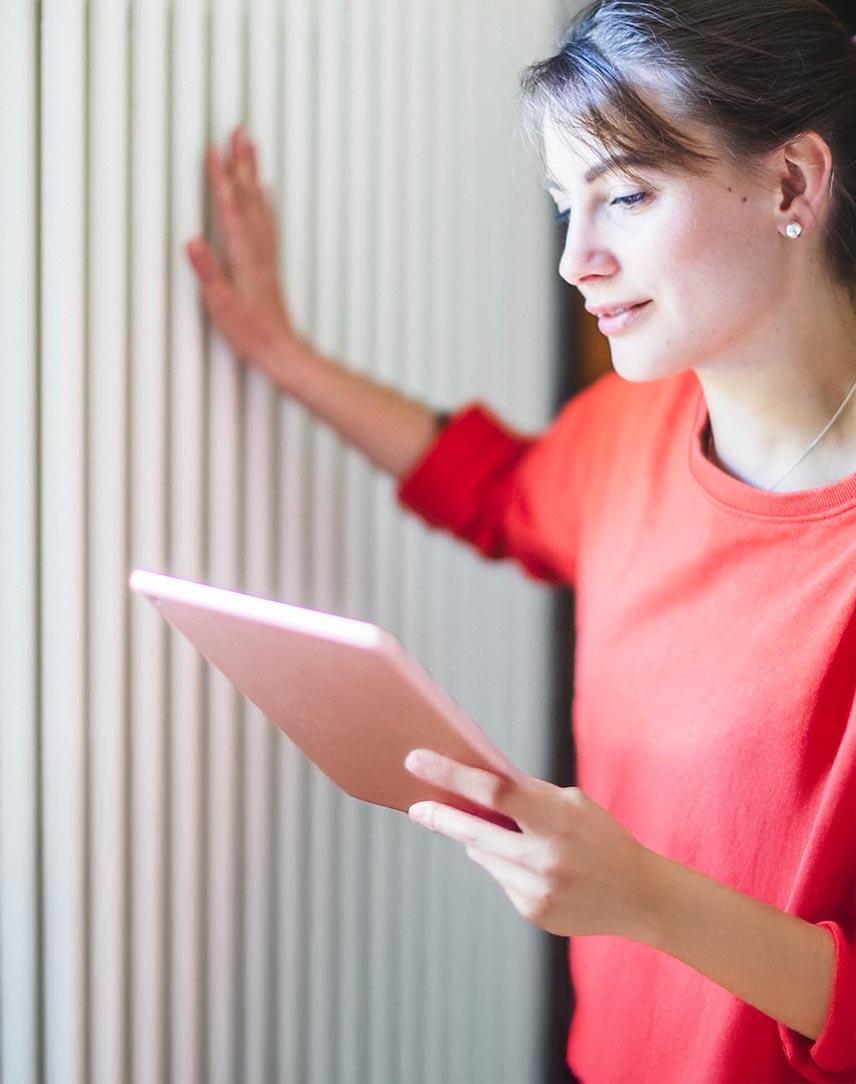 Frau schaut auf ihr Tablet und fühlt die Temperatur der Heizung