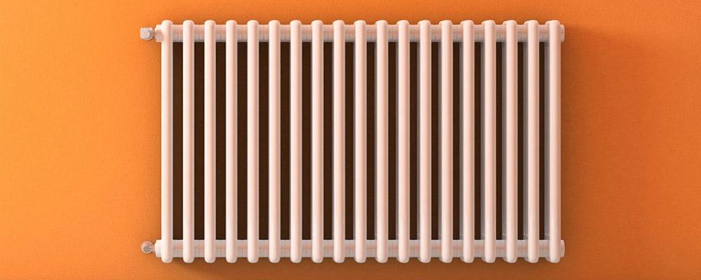 Weißer Gliederheizkörper vor orangefarbener Wand