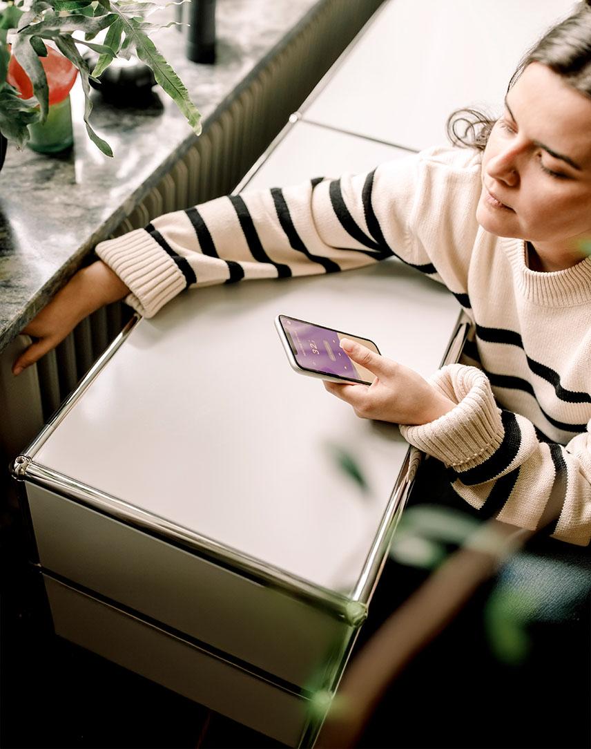 Frau schaut auf ihr Smartphone und fühlt die Temperatur der Heizung