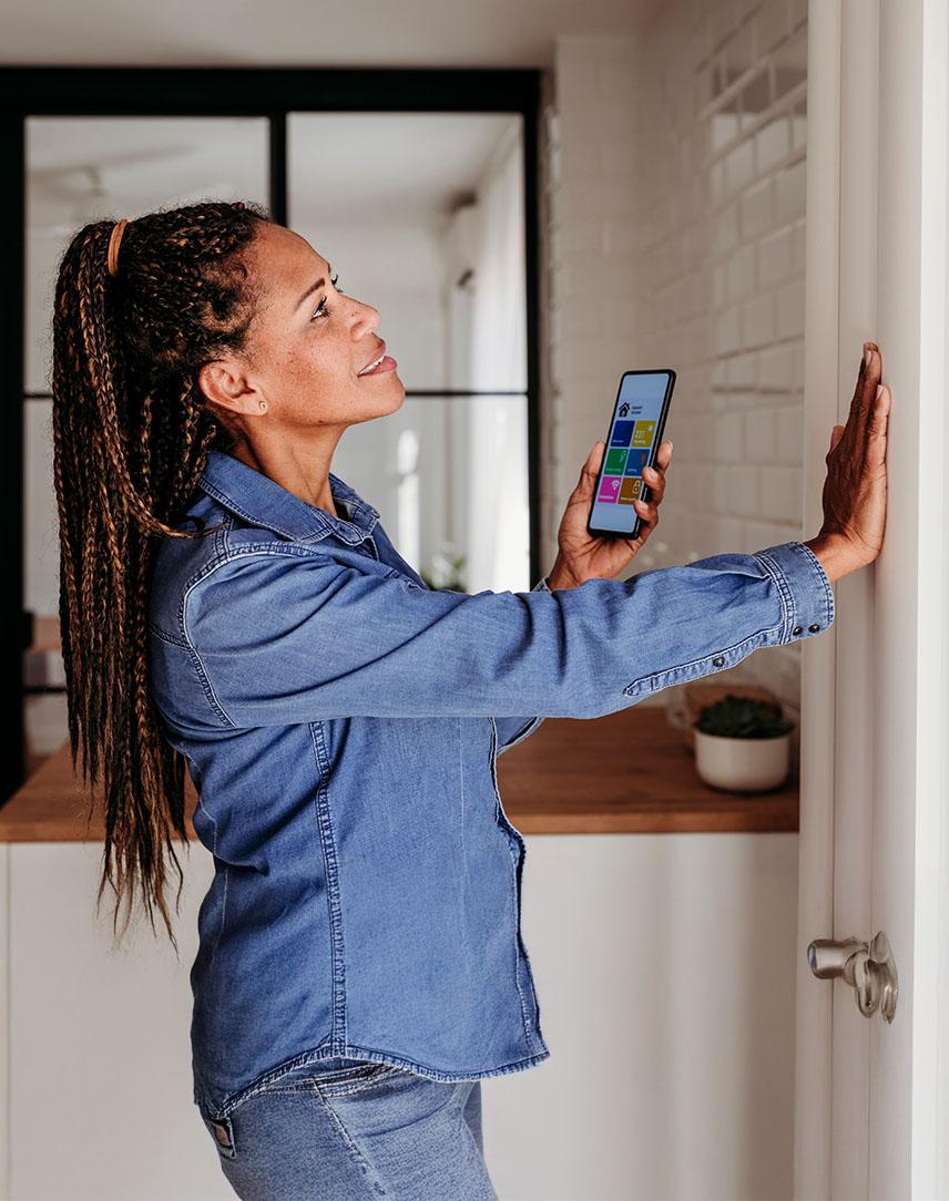 Frau hält Smartphone in der einen Hand und fühlt mit der anderen die Temperatur der Heizung