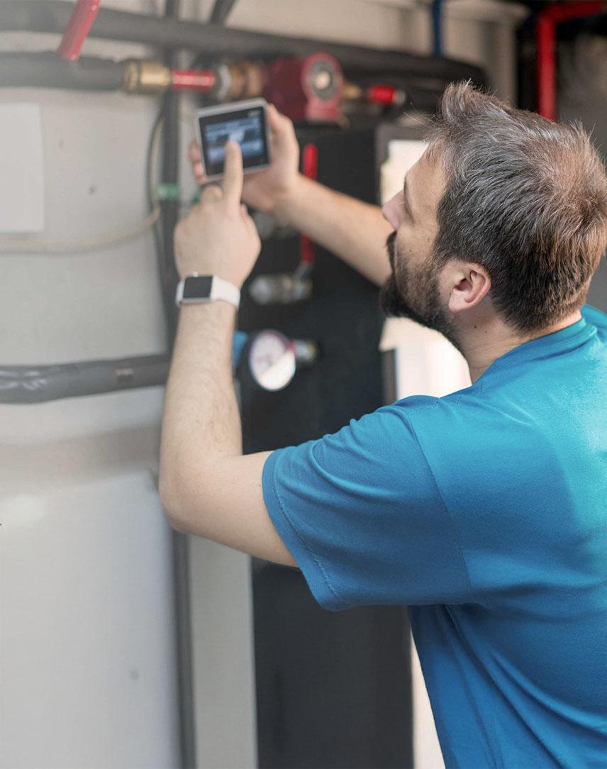 Mann mit Bart schaut auf einen Bildschirm an der Heizungsanlage